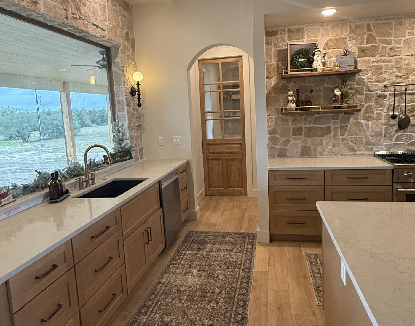 A finished kitchen built with our cabinets — light stained shaker fronts, quartz countertops, stone backsplash, and open shelving